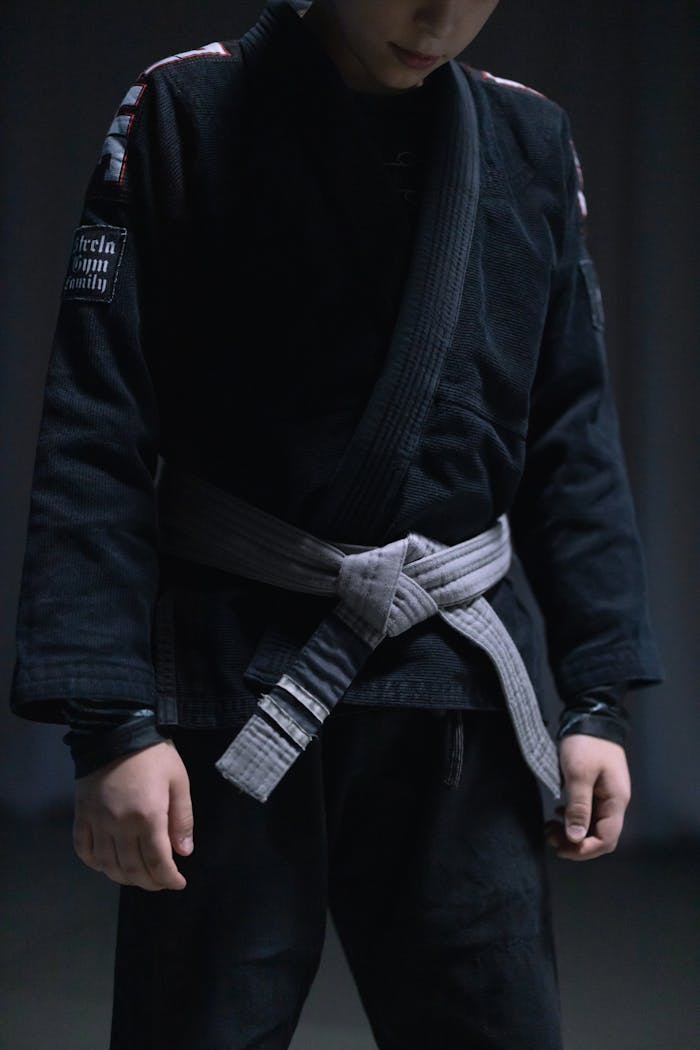 A teenager dressed in a black gi and gray belt, practicing jiu jitsu indoors.